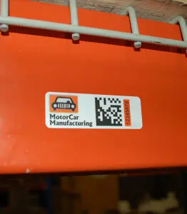 Orange, black, and white label with custom car logo and reading "motorCar Manufacturing" and data matrix code 