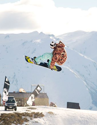 Snowboarder doing a jump with snow covered mountains in the background - rental labels
