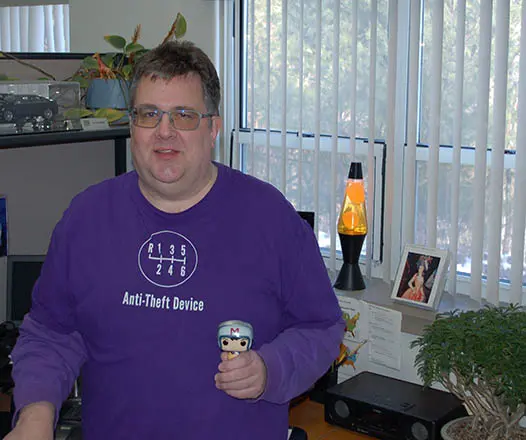 Ed August wearing a purple shirt and glasses holding a toy