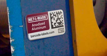 Close-up header image of a Met-L-Mark tag applied to blue and yellow industrial machinery.