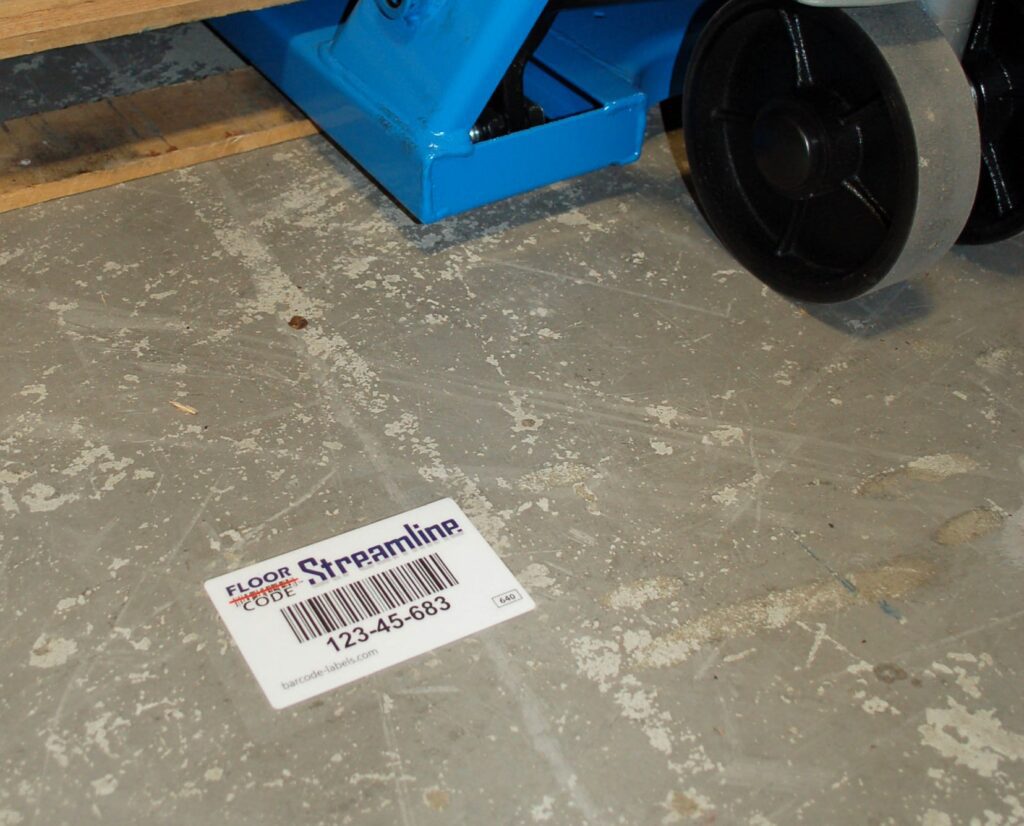 Laminated barcode label on the floor of a warehouse next to a forklift of pallets