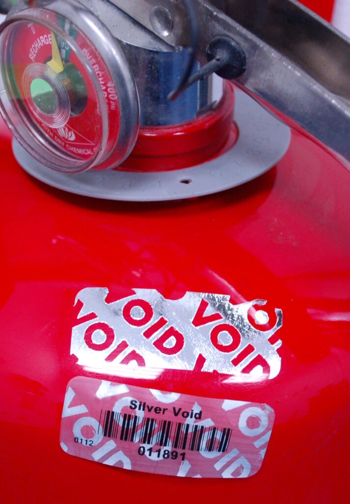 Close-up of a peeled silver VOID label applied to a red fire extinguisher.