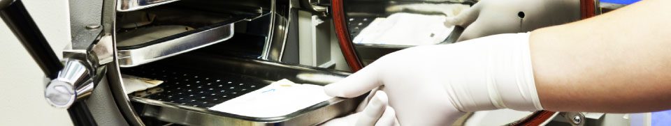 person wearing a rubber glove placing a sheet into an autoclave sterilization machine