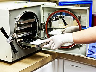 person wearing a rubber glove placing a sheet into an autoclave sterilization machine with lab sterilization labels 