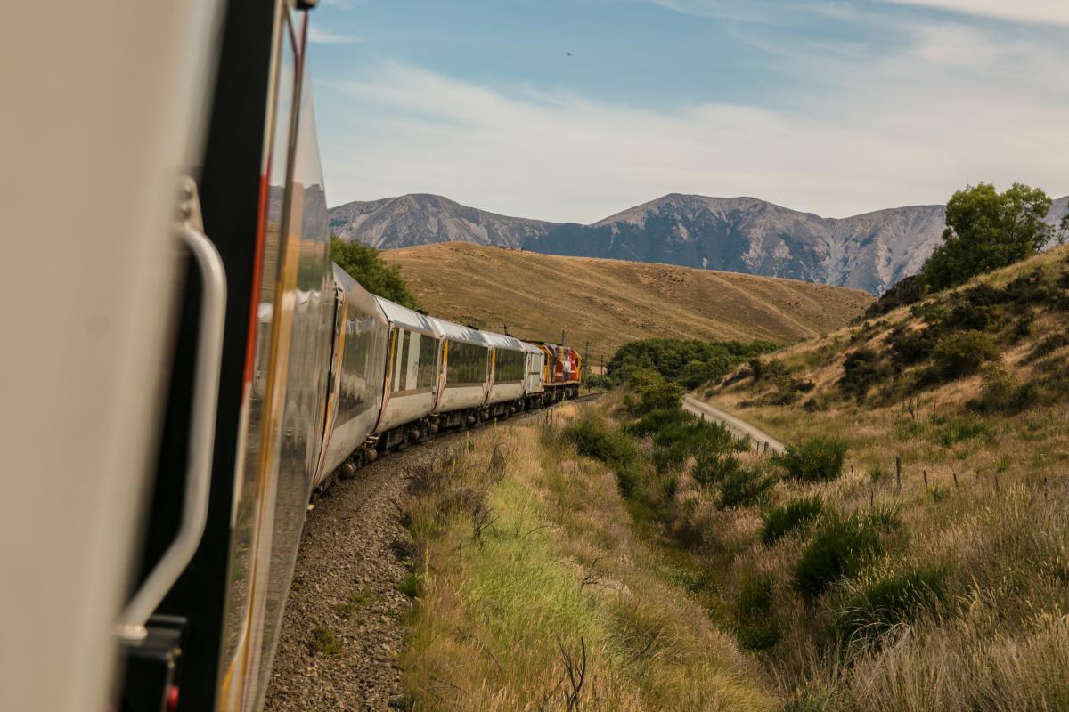 Train winding through grassy hills with mountains in the background 