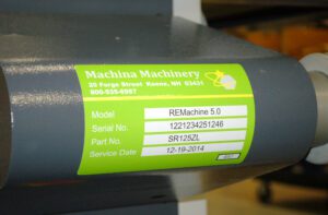 Green vinyl label with model, serial number, part number, and service date affixed to a curved metal surface 