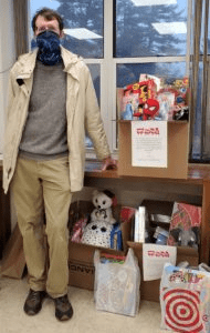masked man standing with toys for tots gifts