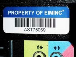White and blue asset label with barcode and "property of EIM Inc" affixed to a black computer - inventory labels