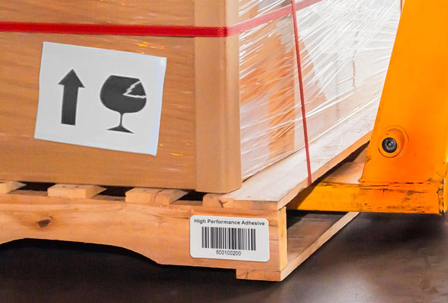 Warehouse worker moving labeled high tack paper wrapped crates on top of a high-performance adhesive labeled wooden pallet