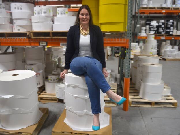 Erin sitting on a stack of blank label roll material inside a warehouse.